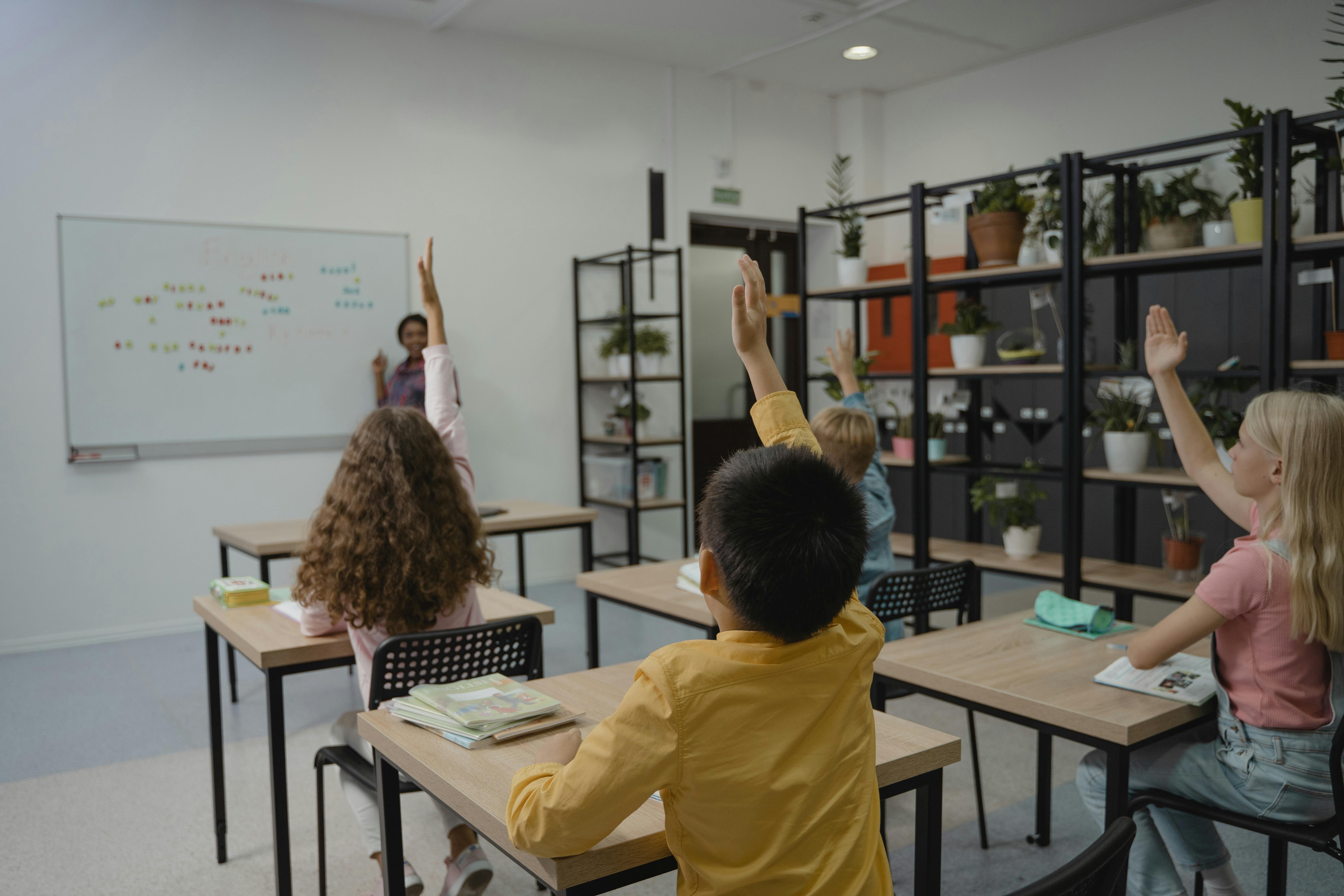 Students raising hands in classroom while school management system supports registers and attendance tracking